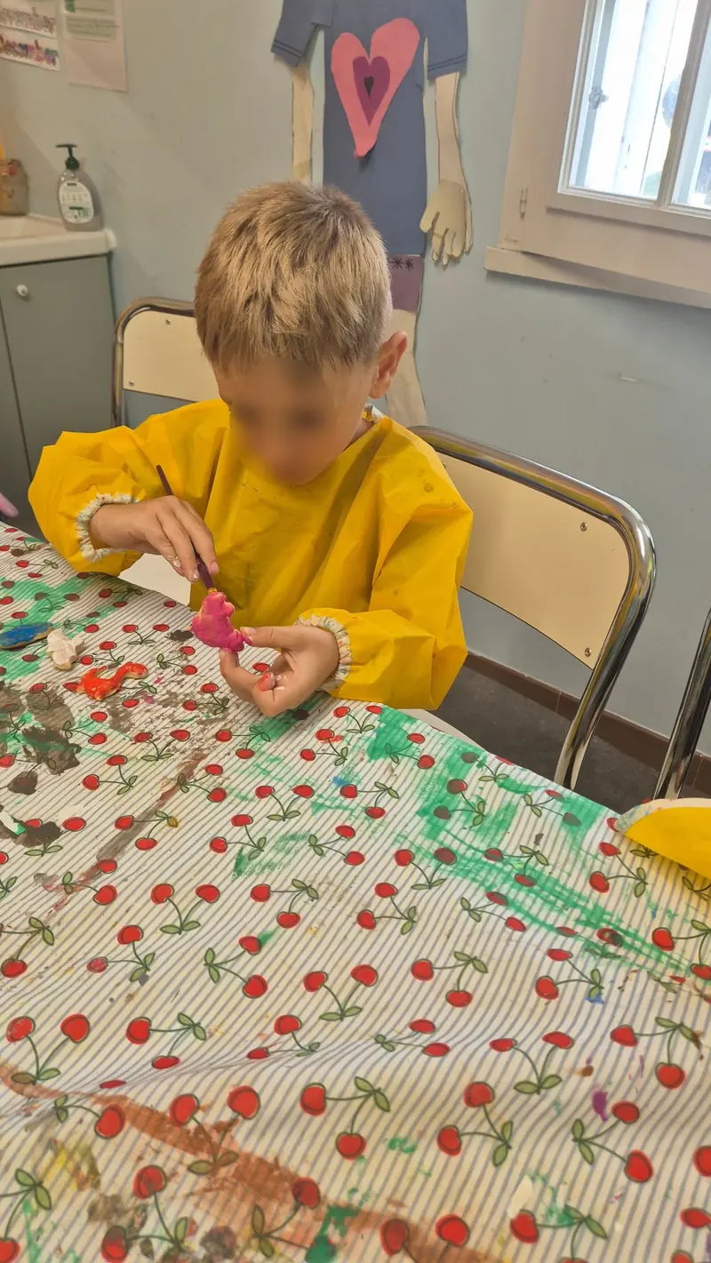 Un enfant en blouse jaune peint une figurine en pâte à sel