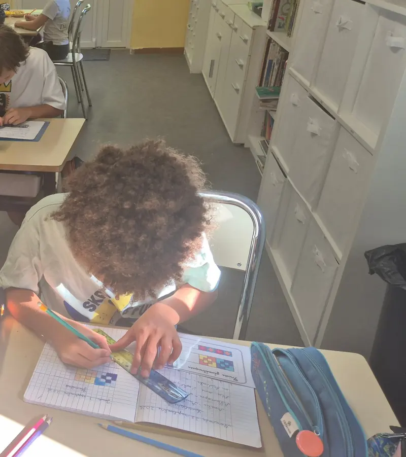 Un enfant penché sur son cahier trace une figure à la règle