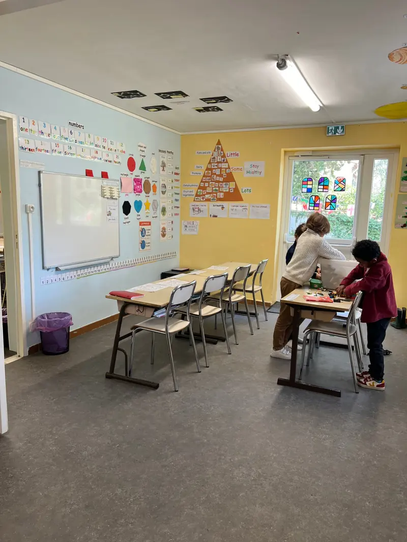 Deux enfants travaillent à une table dans une classe aux murs bleu et jaune