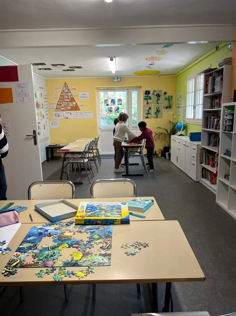 Une classe lumineuse : bibliothèque, puzzle sur la table, enfants au travail au fond