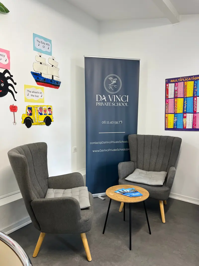 Coin d'accueil avec deux fauteuils, une table basse et des brochures, devant le kakémono Da Vinci Private School