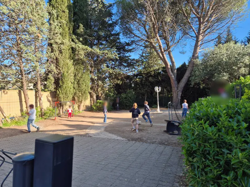 Des enfants jouent au football dans la cour arborée de l'école