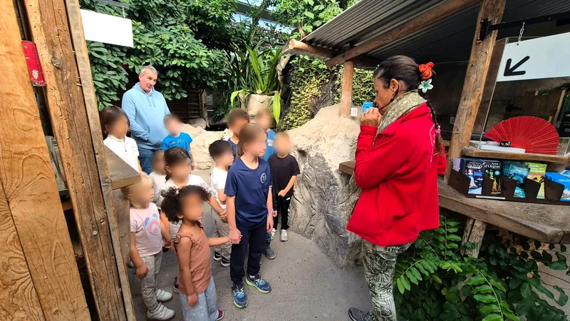Les enfants, petits et grands, se tiennent par la main et écoutent la guide, visages floutés
