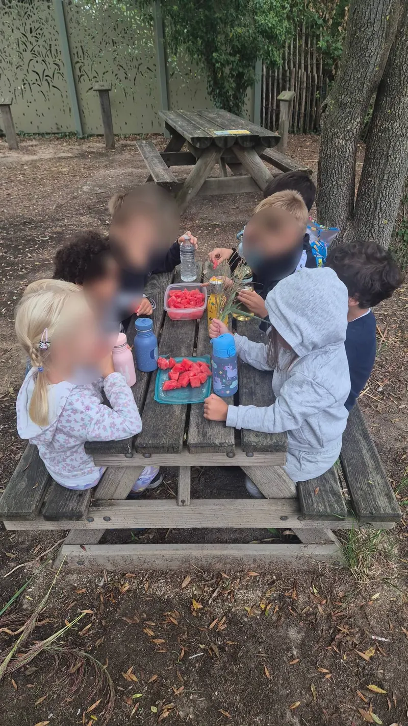 Des enfants partagent de la pastèque autour d’une table de pique-nique en bois