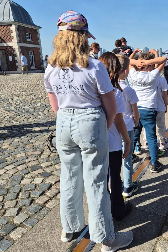 Des enfants de Da Vinci Private School, de dos, alignés sur le méridien de Greenwich lors du voyage à Londres