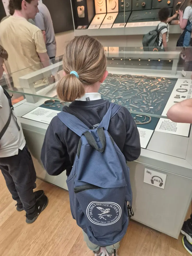 Une enfant, de dos, avec le sac Da Vinci « Offrez-leur le monde », observe une vitrine de musée à Londres