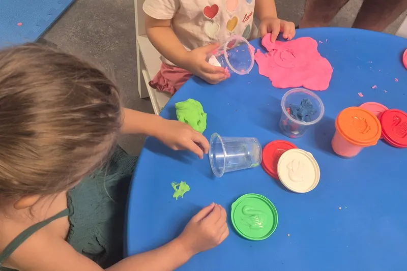 Des mains d'enfants façonnent de la pâte à modeler sur une table bleue
