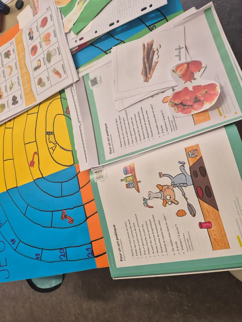 Sur une table de classe : un poème, un loto des fruits et légumes et un jeu de plateau fait main