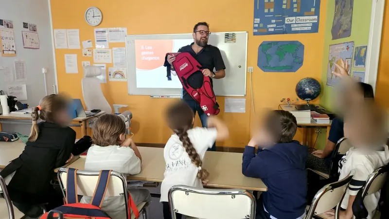 Jonathan Filiu, a first aid trainer, showing a first aid bag to children raising their hands, in front of the “emergency actions” slide