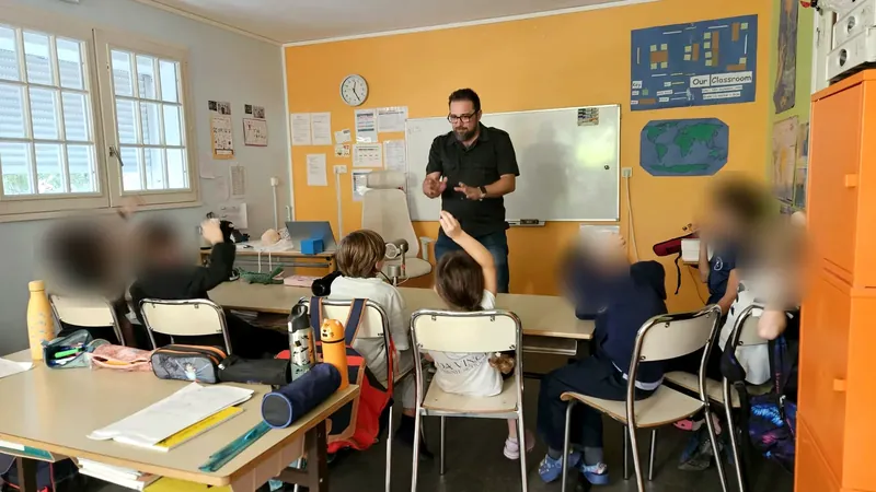 Children, seen from behind, raising their hands to answer the trainer during the first aid workshop